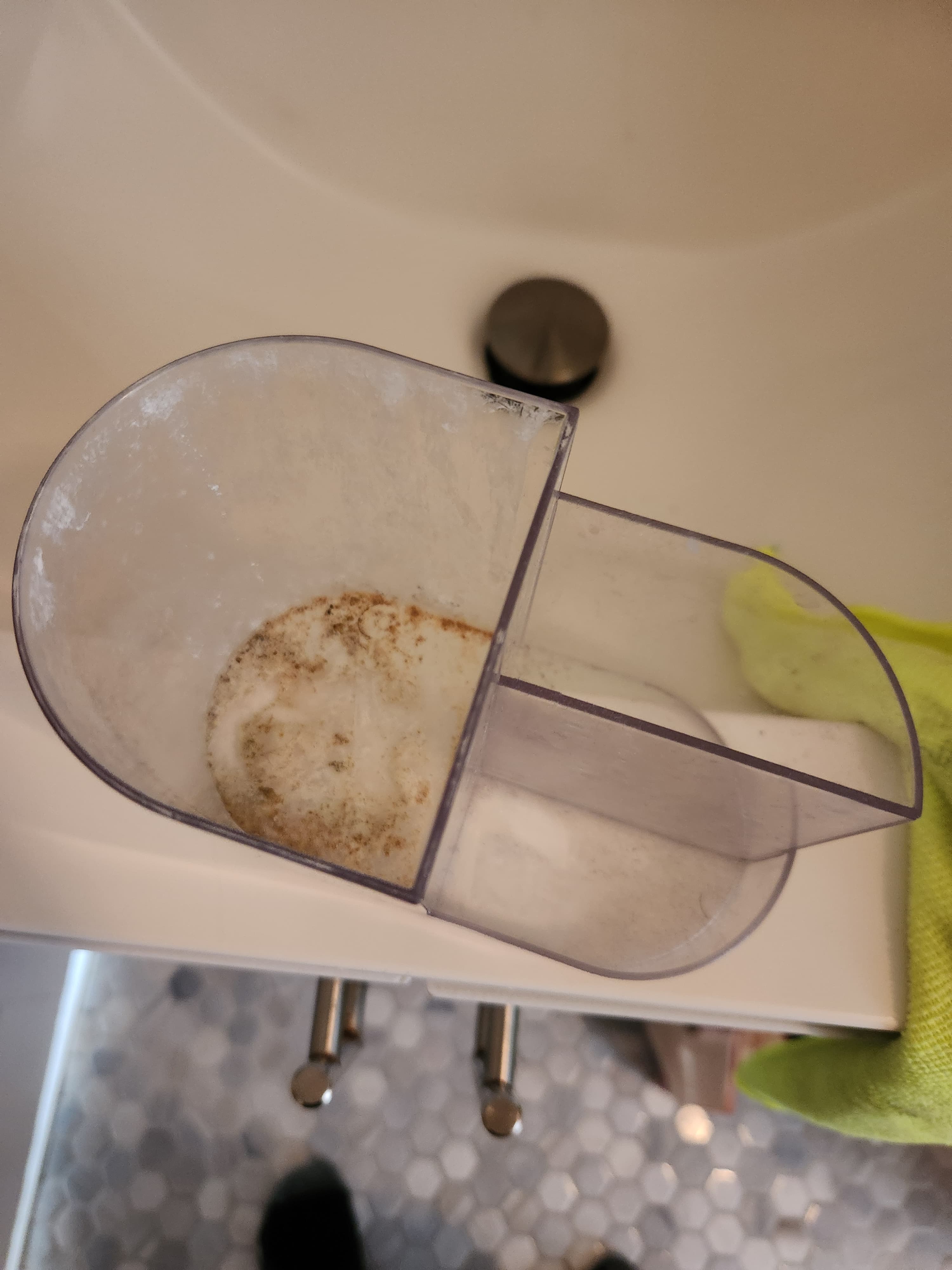 Clear plastic water reservoir with brown mold and mineral buildup on a white sink.