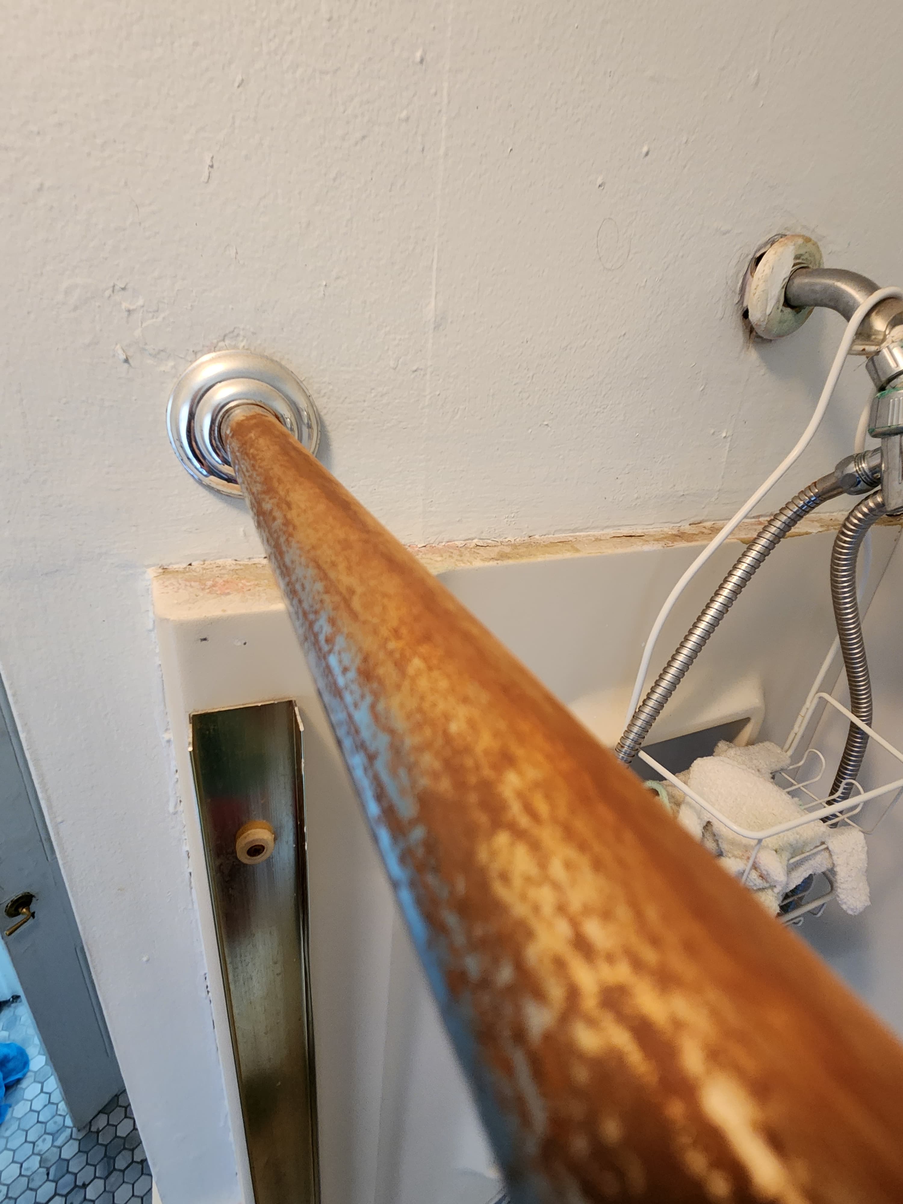 A heavily rusted metal shower curtain rod mounted to a white wall in a bathroom.