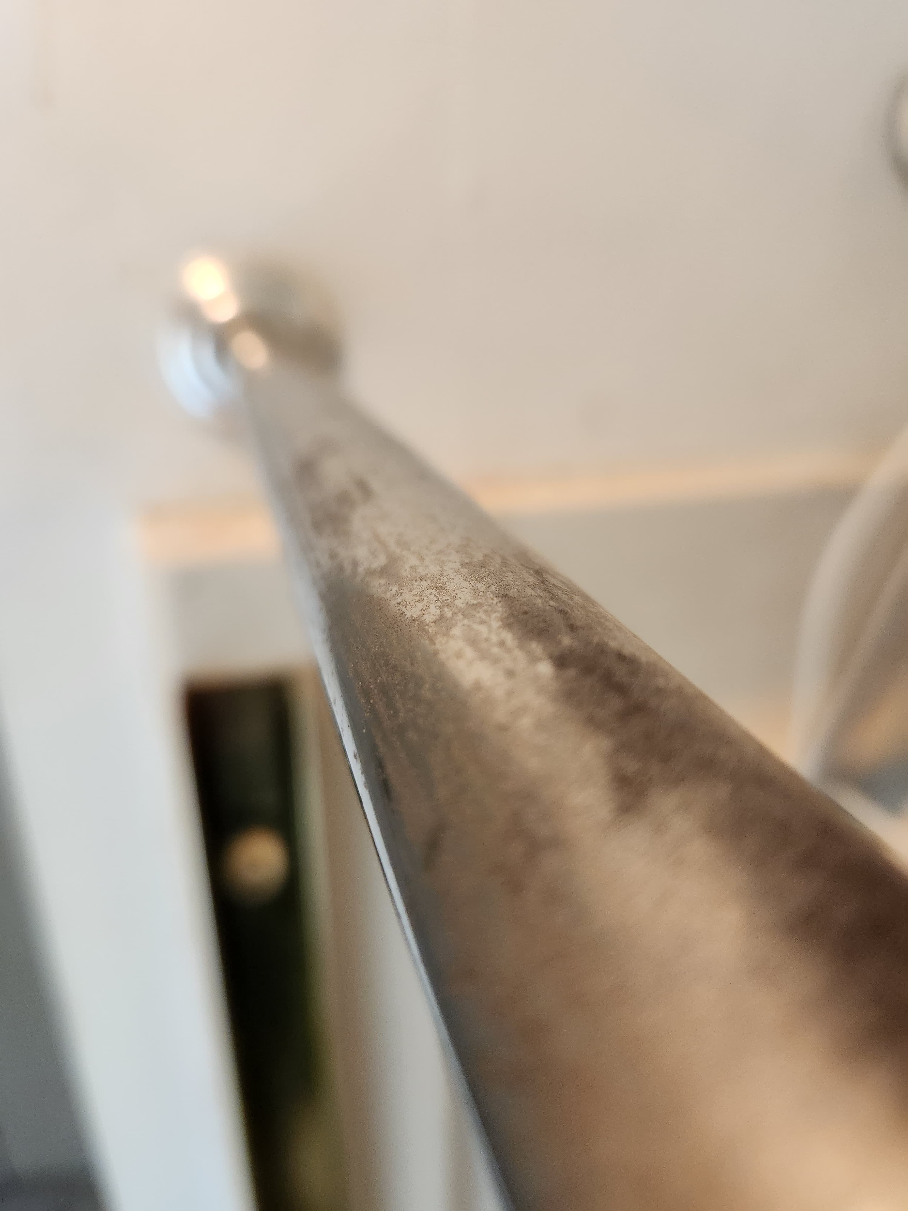 Close-up perspective of a tarnished metal rod covered in dark grime and water spots.