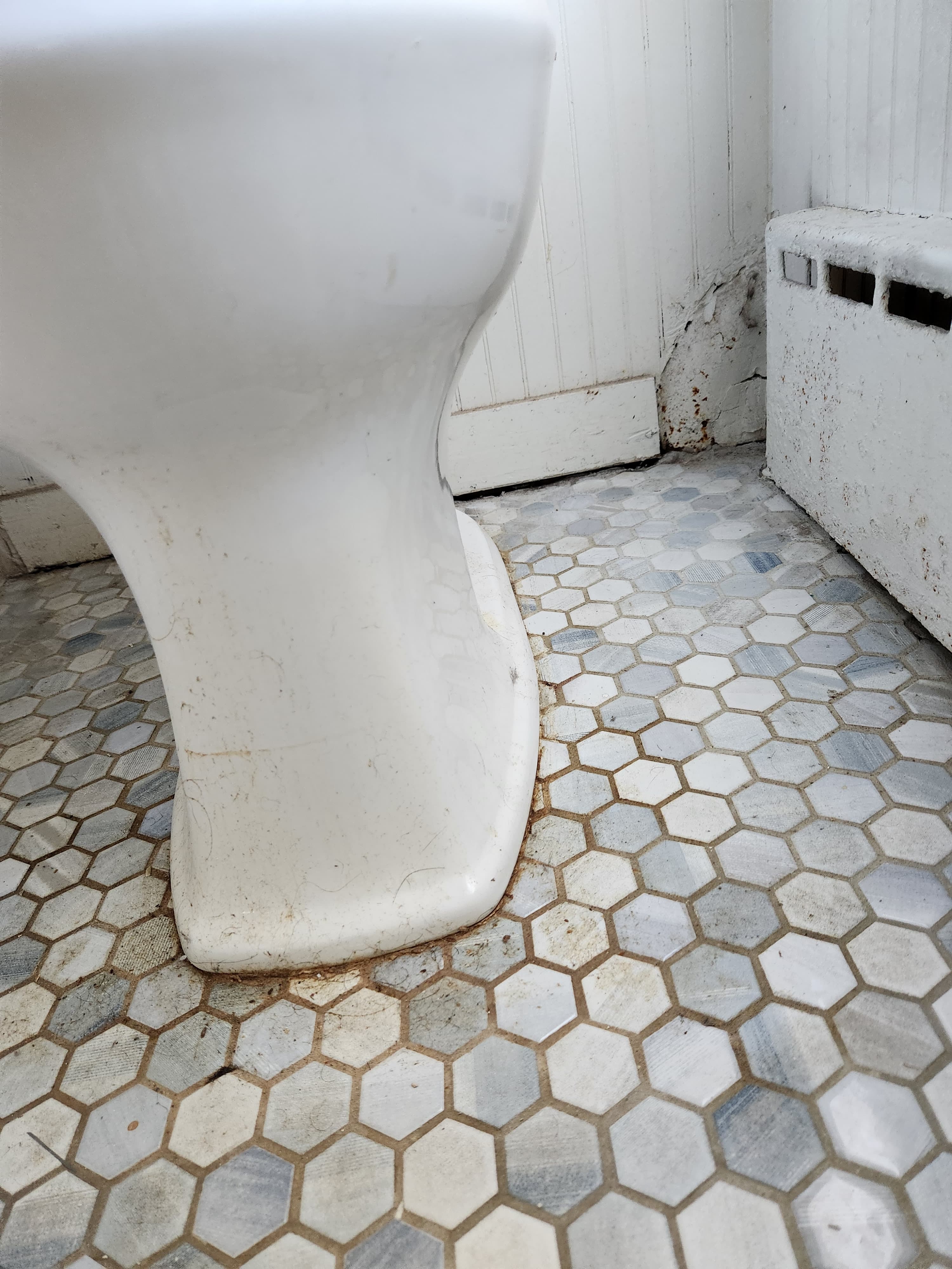Dirty white toilet base on a blue and white hexagonal tile floor with visible grime.
