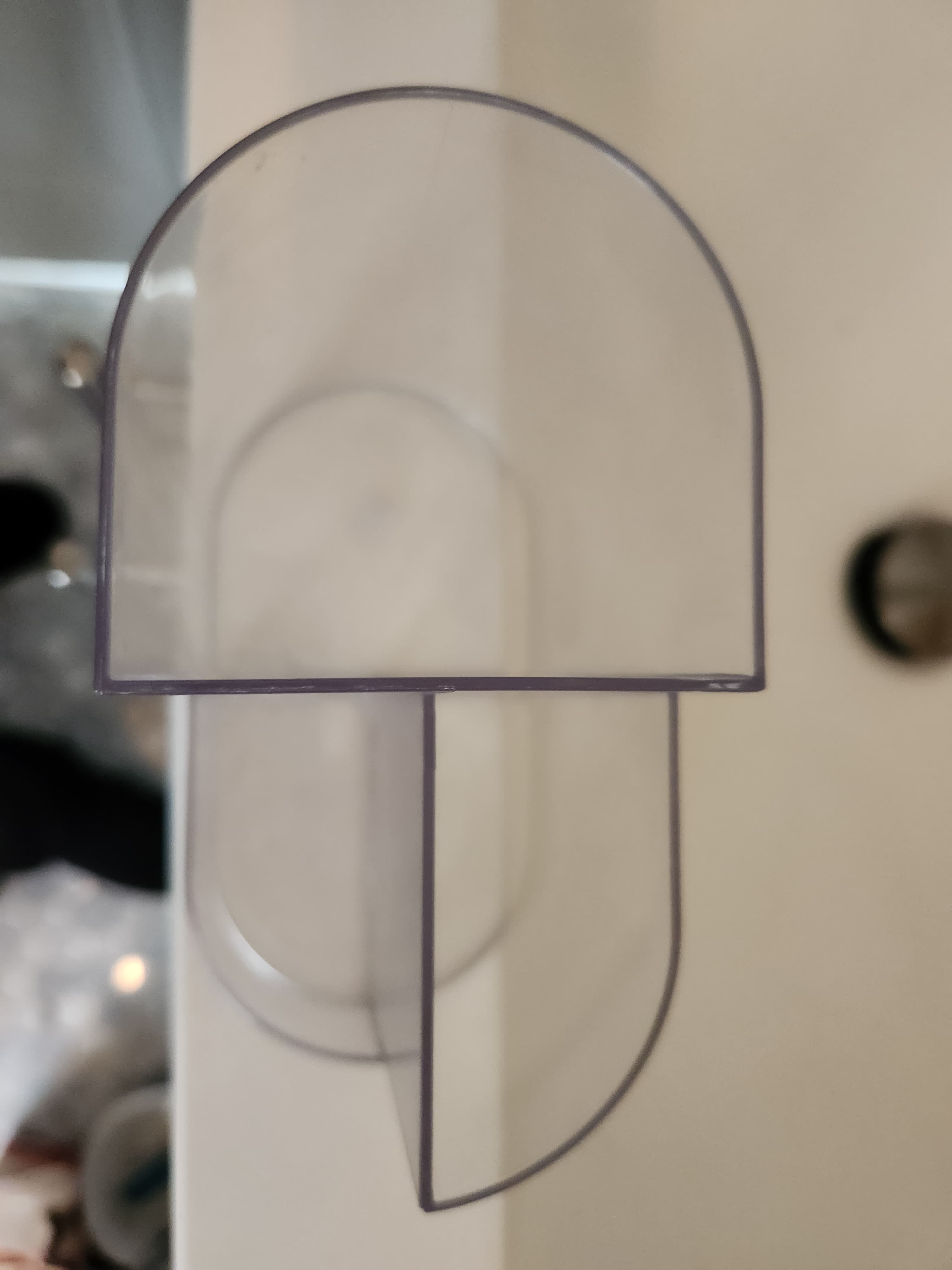 Transparent plastic component with a semi-circular top and vertical divider on a white surface.
